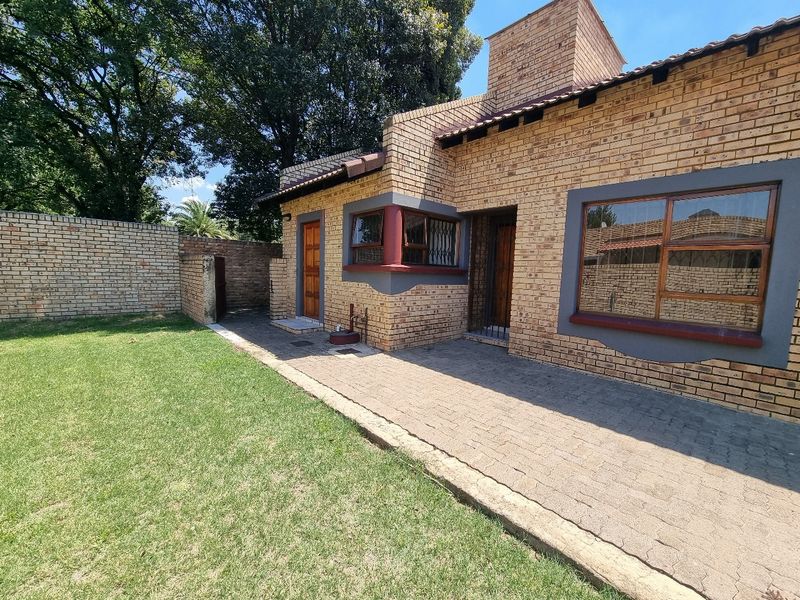 Rear view of the townhouse featuring a face brick facade, a paved patio area, and a private garden with a surrounding boundary wall.