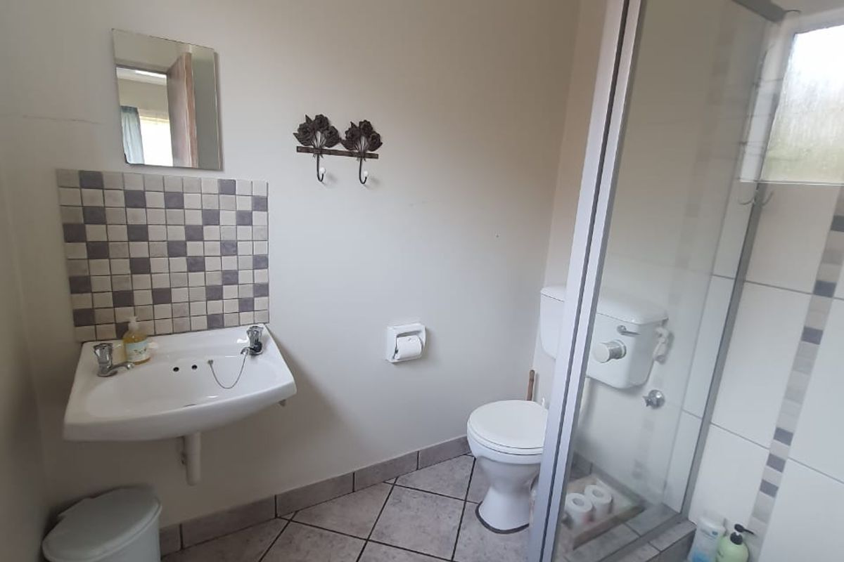 A functional bathroom featuring a glass-enclosed shower, wall-mounted basin with mosaic splashback, and a standard toilet with tiled flooring.