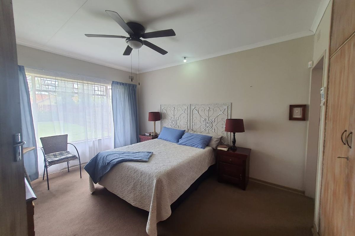 A standard bedroom featuring a ceiling fan, large window with natural light, and built-in wooden cupboards.