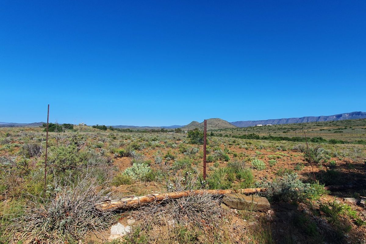 A wide-angle view of vacant residential land featuring natural scrub vegetation, distant mountain ranges, and existing wire perimeter fencing.
