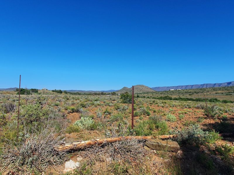 A wide-angle view of vacant residential land featuring natural scrub vegetation, distant mountain ranges, and existing wire perimeter fencing.