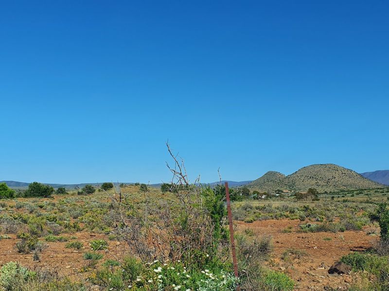 A wide-angle view of the vacant residential land featuring natural scrub vegetation and distant mountain scenery.