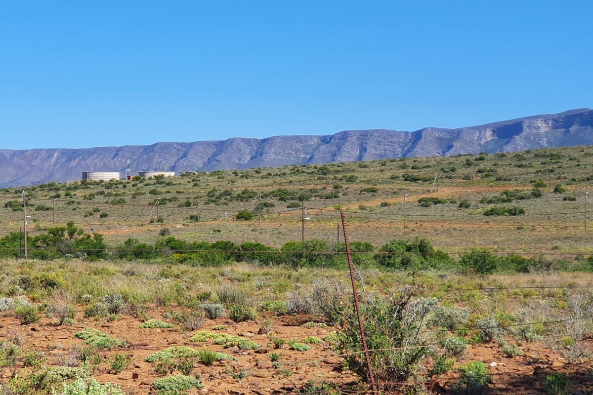 A scenic view of the expansive vacant land featuring natural vegetation, wire fencing, and distant mountain ranges under a clear blue sky.