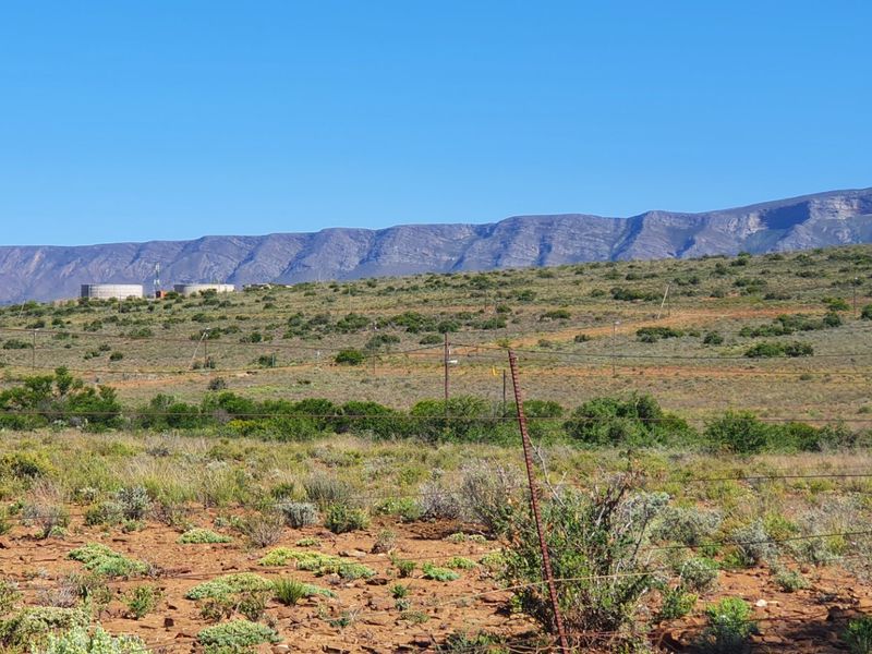 A scenic view of the expansive vacant land featuring natural vegetation, wire fencing, and distant mountain ranges under a clear blue sky.