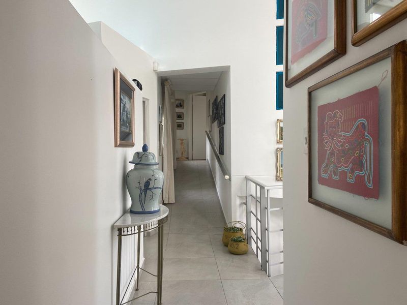 A bright, well-maintained hallway featuring tiled flooring and a metal handrail, leading towards a secondary corridor area.