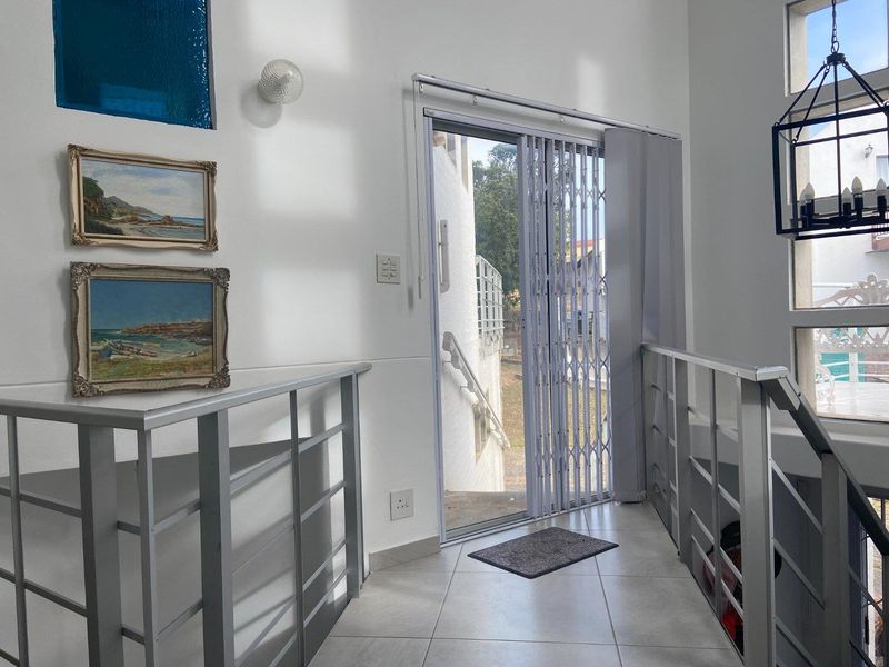 A bright hallway featuring tiled flooring, metal staircase railings, and a sliding glass door with a security gate leading to the exterior.