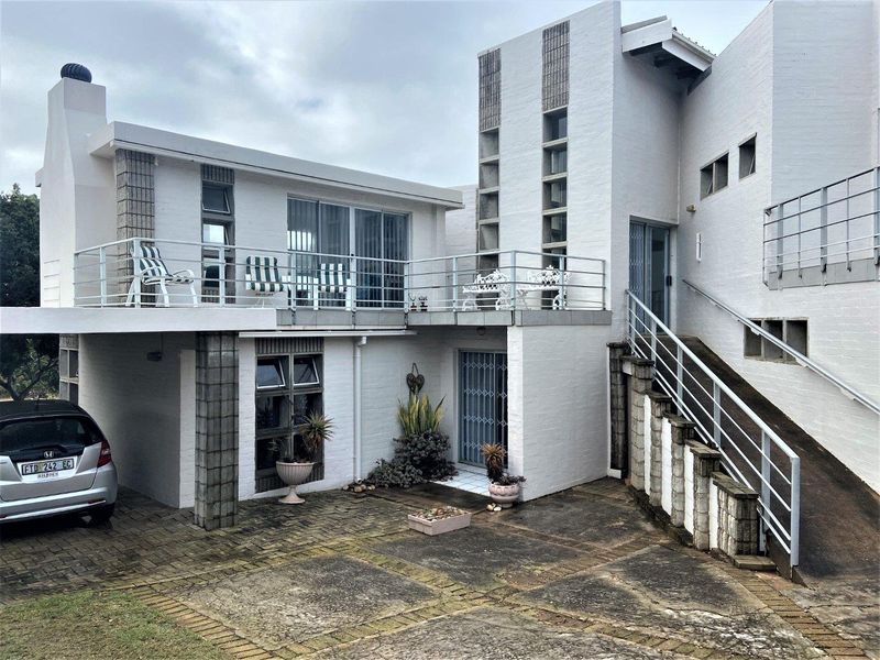Front elevation of a multi-level house featuring a paved driveway, covered parking, an elevated balcony with metal railings, and an external staircase.