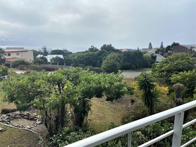An elevated view overlooking a residential neighborhood with mature trees and distant coastal scenery, captured from a balcony.