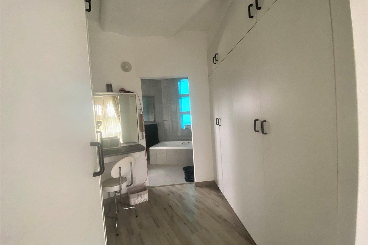 A dressing area featuring extensive built-in cupboards and laminate flooring, leading directly into an en-suite bathroom.