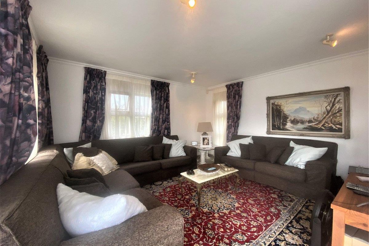 A comfortable living room featuring neutral walls, coving, and multiple windows that provide natural light.