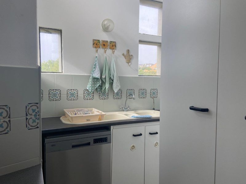 A functional scullery area featuring a double basin sink, tiled backsplash, and built-in cabinetry with an integrated dishwasher.