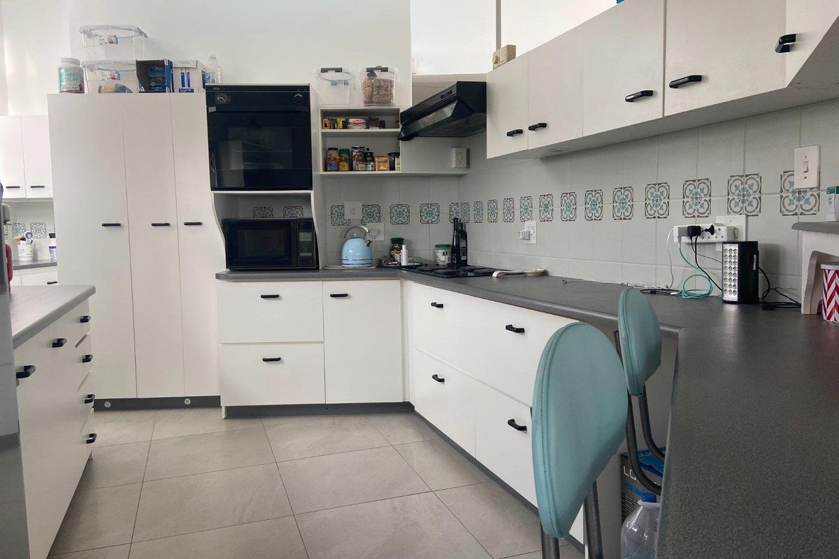 A functional kitchen featuring white cabinetry, dark laminate countertops, a built-in oven, extractor fan, and decorative tiled backsplash with neutral floor tiling.