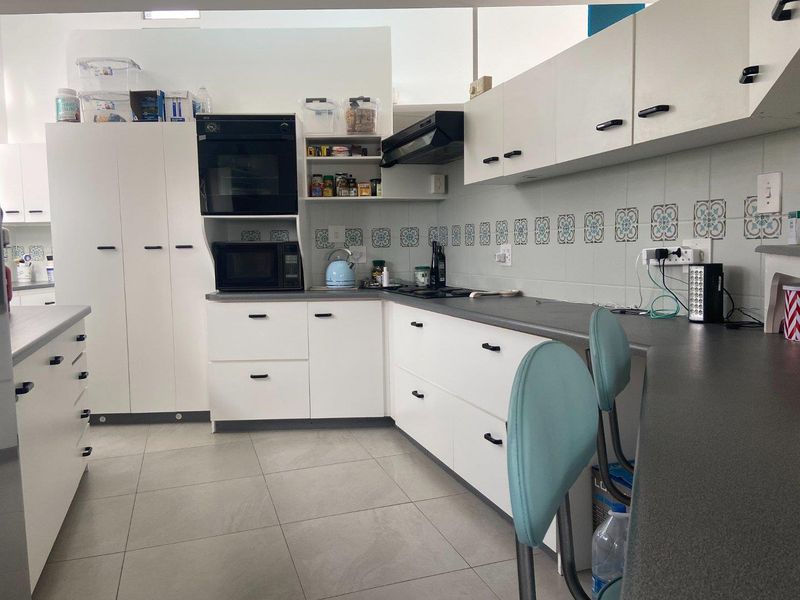 A functional kitchen featuring white cabinetry, dark laminate countertops, a built-in oven, extractor fan, and decorative tiled backsplash with neutral floor tiling.