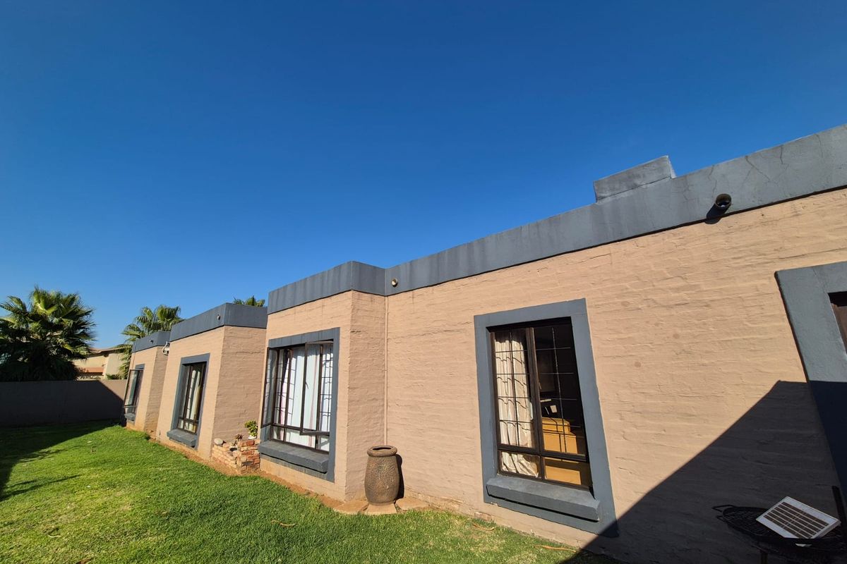 A view of the rear exterior facade of the house, featuring painted brick walls, dark window frames, and a well-maintained lawn area.