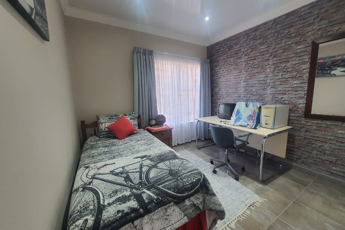 A bedroom featuring a textured brick accent wall, tiled flooring, and recessed ceiling lighting, offering a functional space with neutral wall finishes.