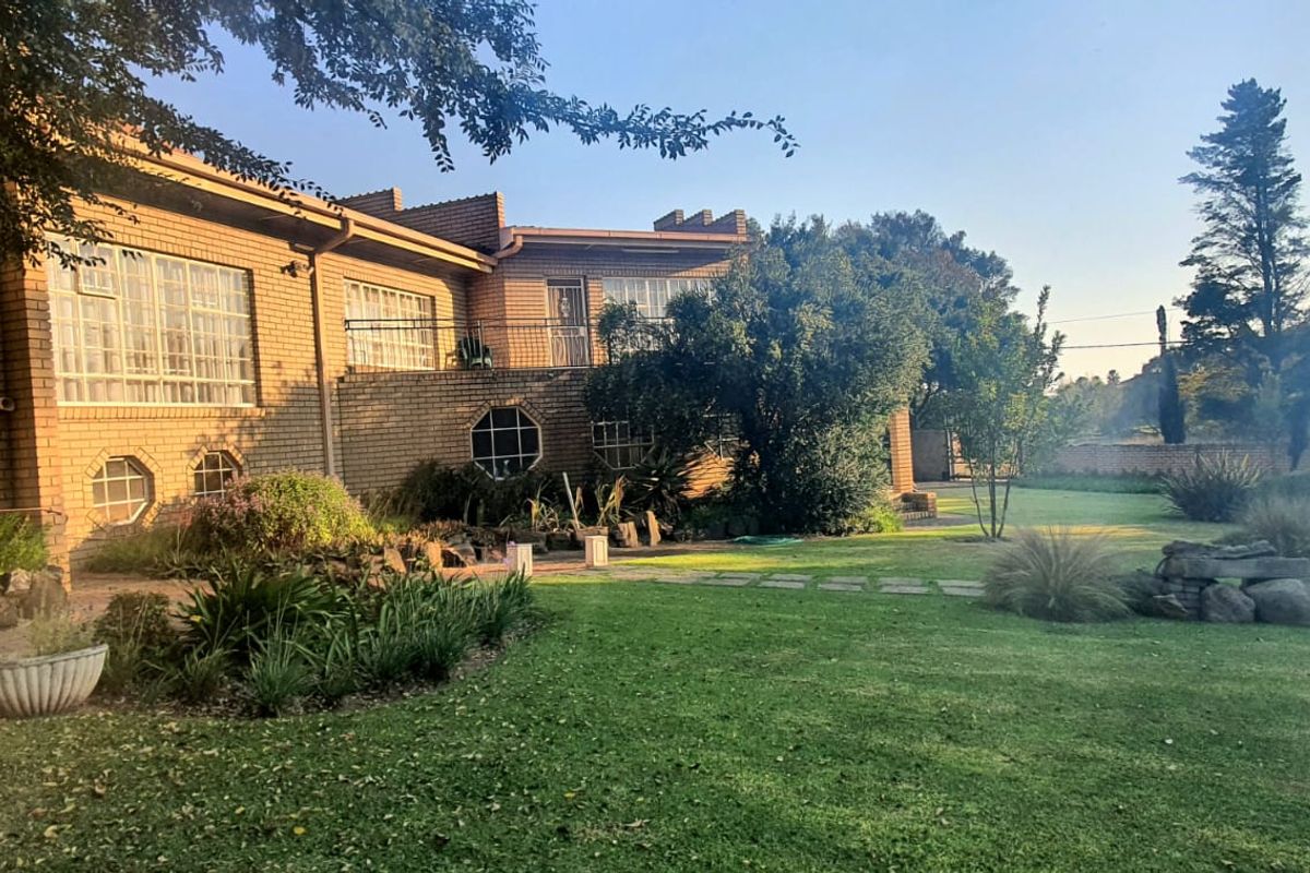 A view of the rear brick facade of the house, featuring a landscaped garden with established trees, lawn, and stone garden beds.
