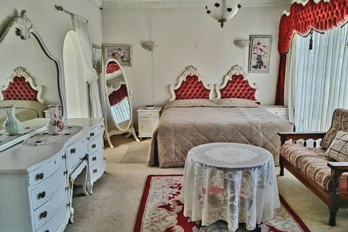 A spacious bedroom featuring ornate crown molding, decorative wall sconces, and large windows with heavy drapery.