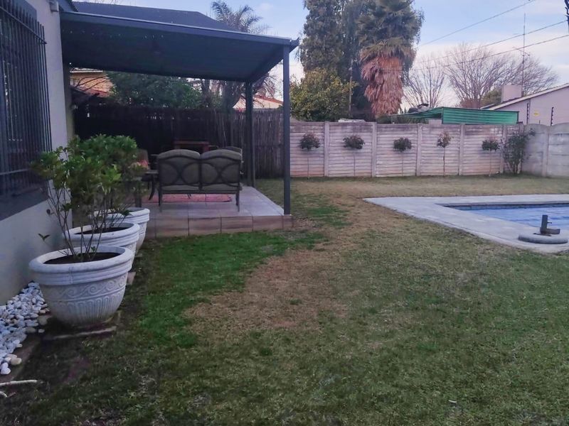 Rear garden featuring a covered patio area, a swimming pool, and a secure boundary wall.