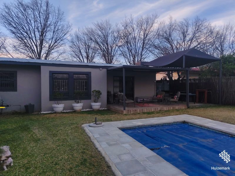 Rear view of the property featuring a covered patio area, a swimming pool with a cover, and a landscaped garden.