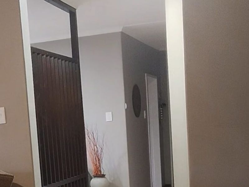 A well-lit hallway featuring tiled flooring and a decorative timber slat room divider, providing a clean transition between living spaces.