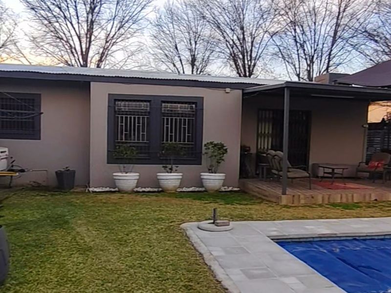 Rear view of the property featuring a swimming pool with a paved surround, a covered patio area, and a well-maintained lawn.