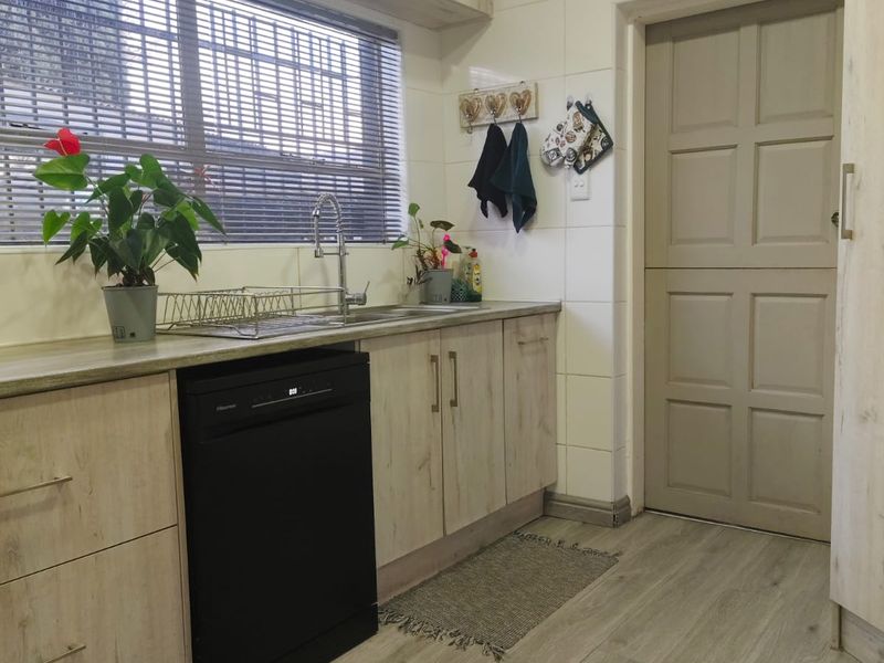 A functional kitchen featuring light wood-look cabinetry, laminate countertops, a stainless steel sink, and durable laminate flooring with a classic panelled door.