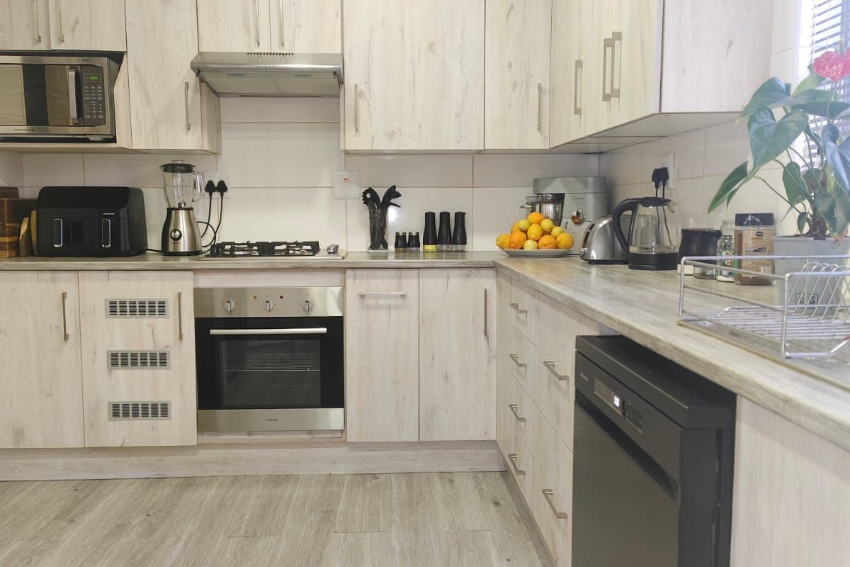 Modern kitchen featuring light wood-grain cabinetry, laminate countertops, built-in oven, gas hob, and integrated dishwasher with durable laminate flooring.