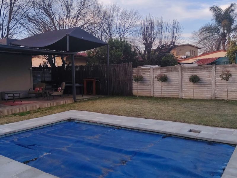 Outdoor pool area featuring a paved surround, a blue pool cover, and an adjacent covered patio space within a fenced garden setting.