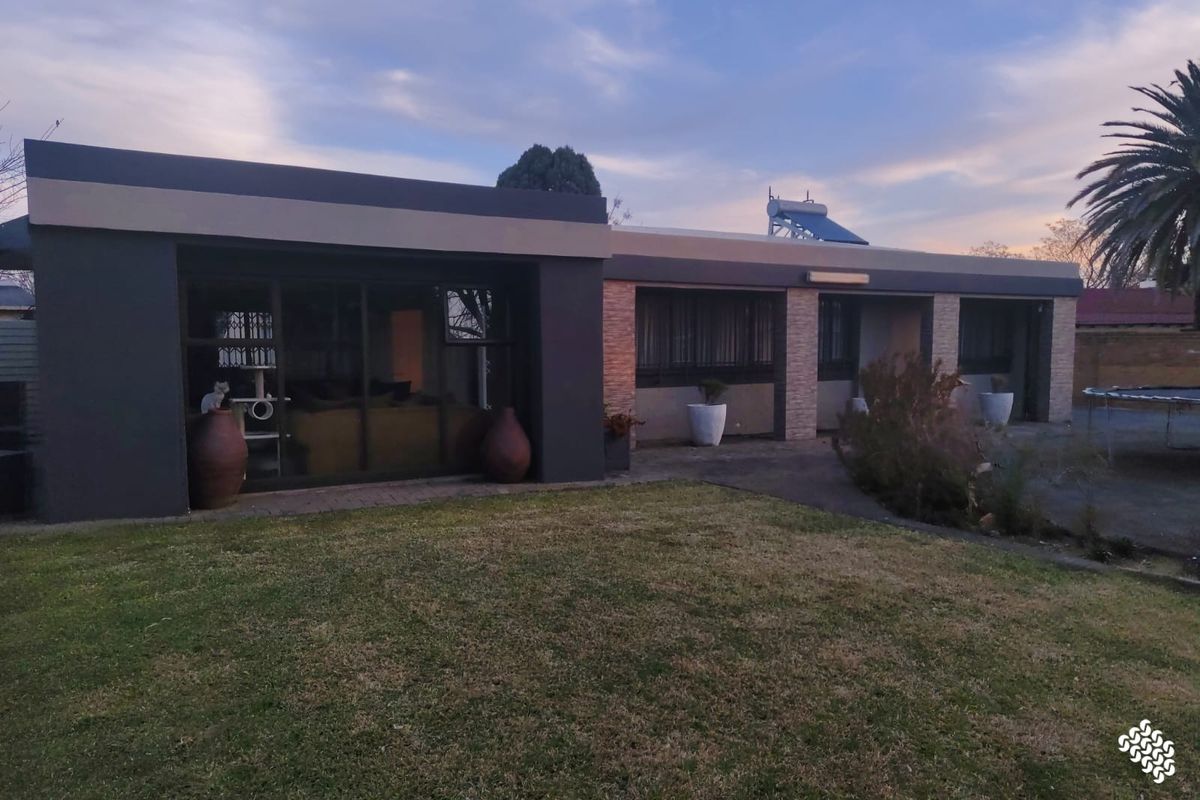 Rear view of the property featuring a paved patio area, lawn, and modern exterior finishes with a solar water heating system installed on the roof.
