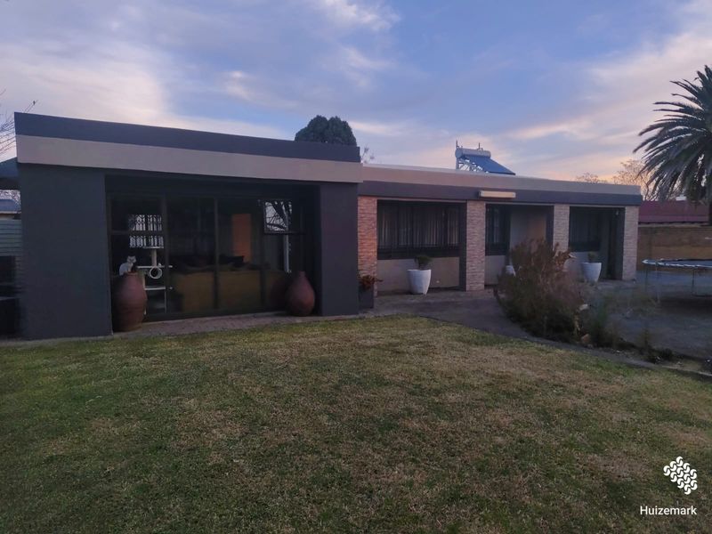 Rear view of the property featuring a paved patio area, lawn, and modern exterior finishes with a solar water heating system installed on the roof.