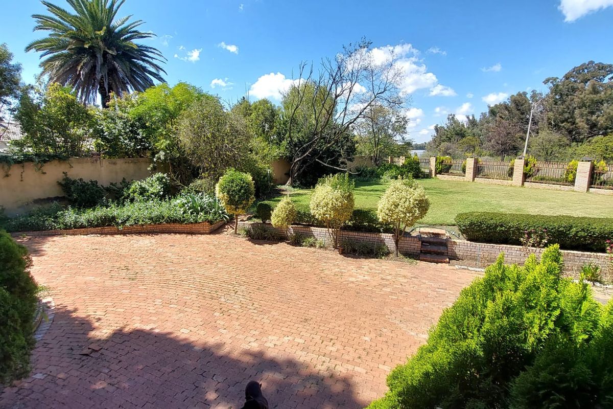 A spacious rear garden featuring a large brick-paved patio area, manicured lawn, established landscaping, and perimeter boundary walls.