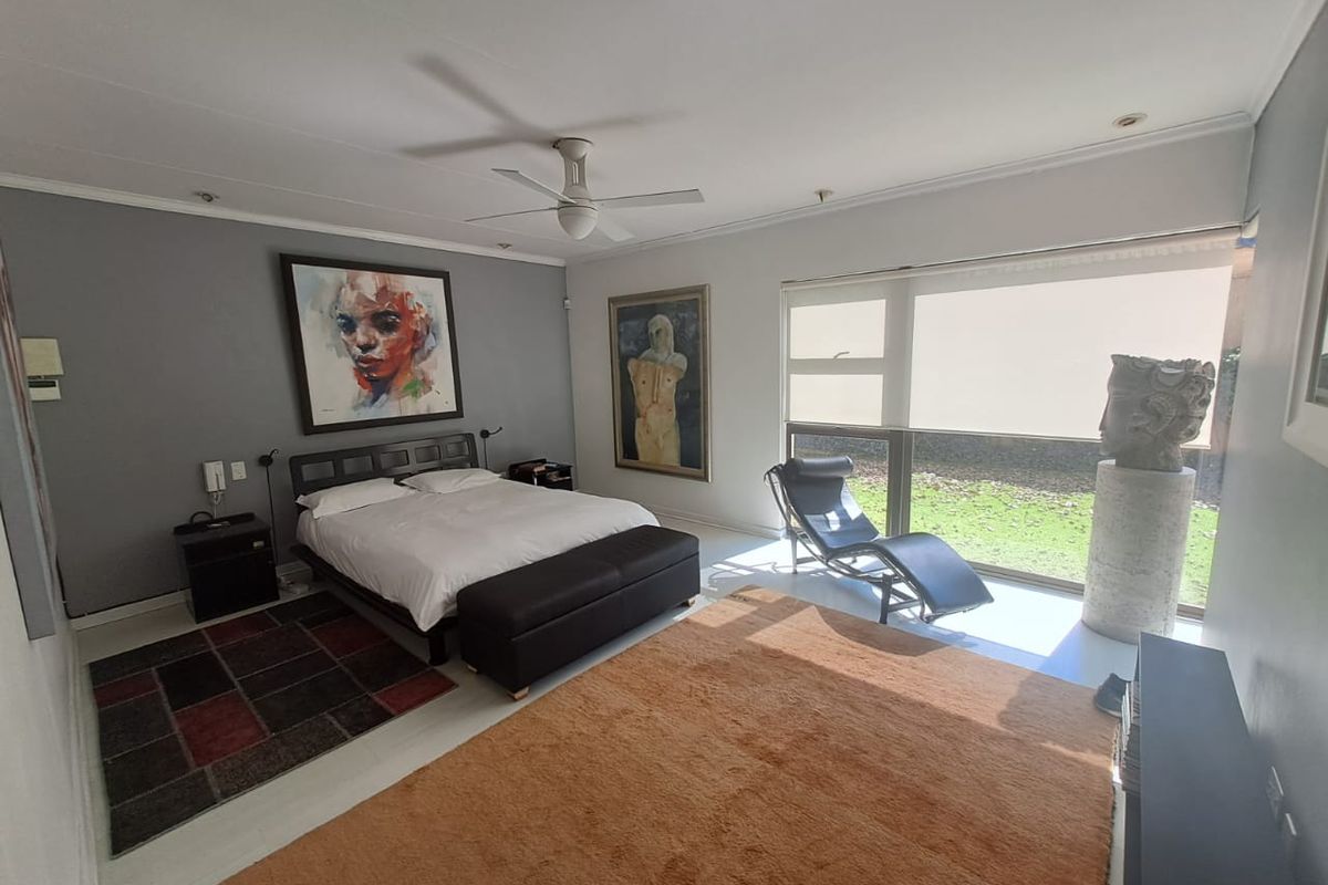 Spacious bedroom featuring large windows with garden views, a ceiling fan, and neutral wall finishes.