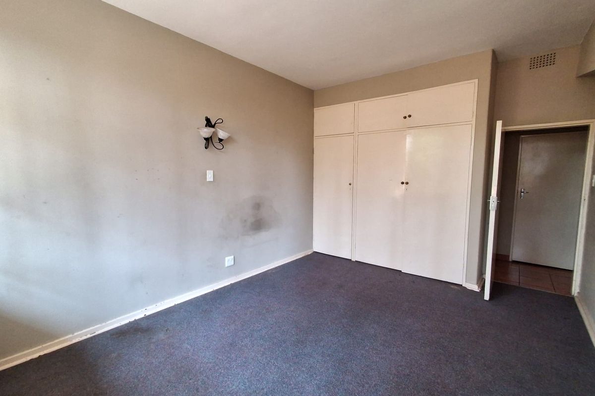 A vacant bedroom featuring built-in cupboards, wall-mounted lighting, and carpeted flooring, presenting a blank canvas for renovation.