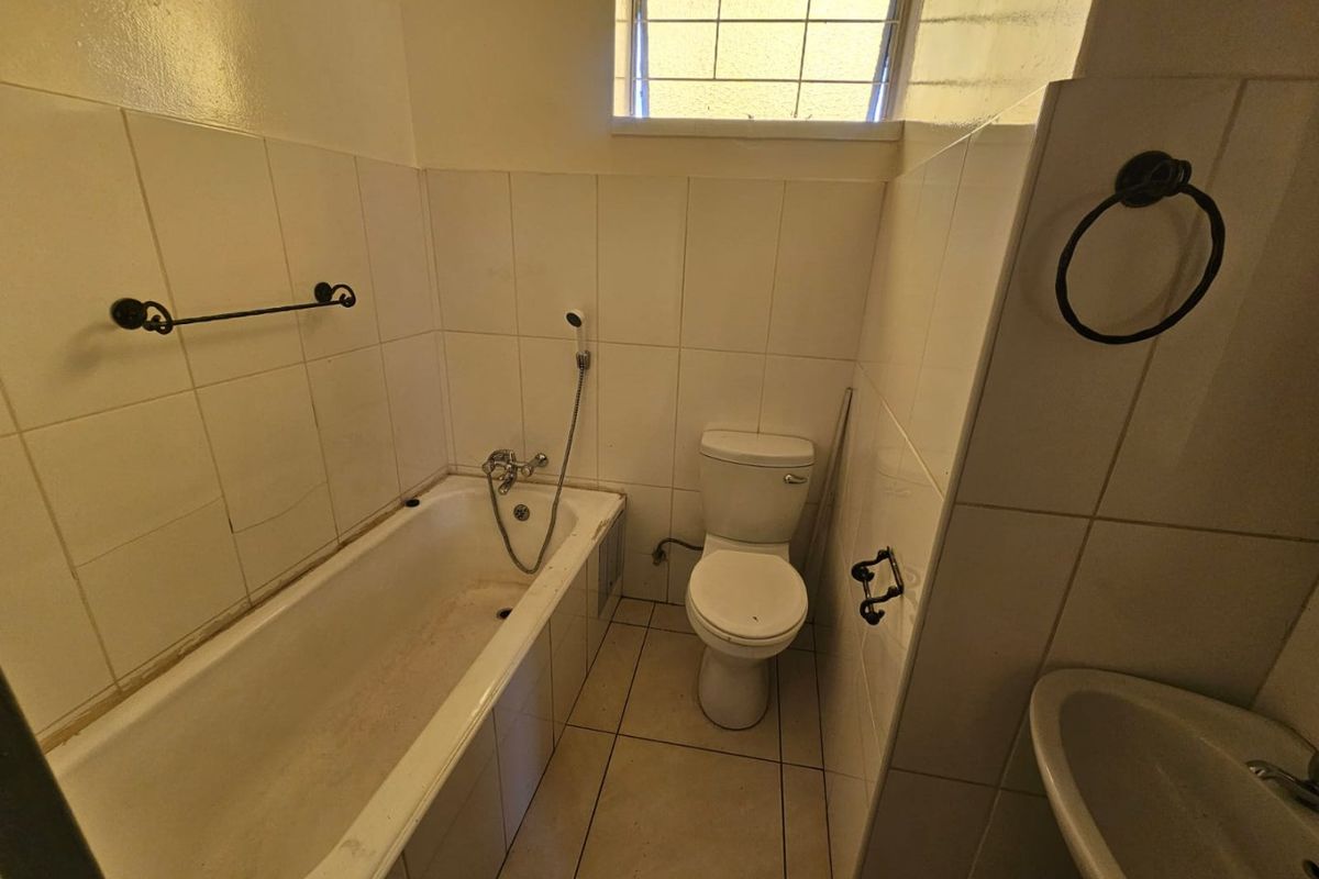 A compact bathroom featuring a bathtub with handheld shower, a standard toilet, and a wall-mounted basin with tiled walls and flooring.