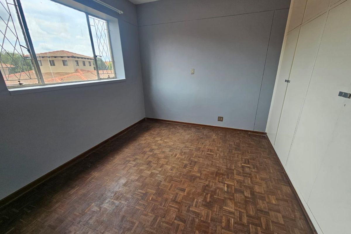 A vacant bedroom featuring original parquet flooring, built-in cupboards, and large windows providing natural light.