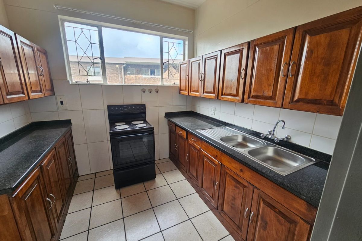 A functional kitchen featuring traditional wooden cabinetry, dark countertops, a double-basin sink, and a freestanding stove, set against tiled flooring and splashbacks.