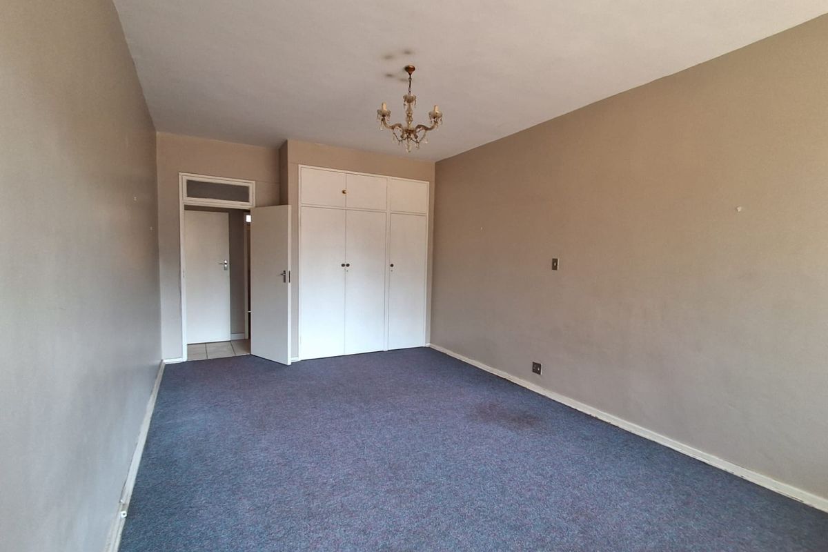 A spacious, empty bedroom featuring built-in cupboards, neutral wall tones, and carpeted flooring, offering a blank canvas for personalization.