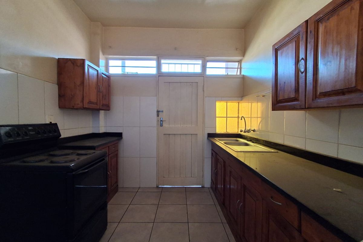 A functional kitchen featuring wooden cabinetry, dark countertops, a built-in stove, and tiled flooring with direct access to an exterior door.