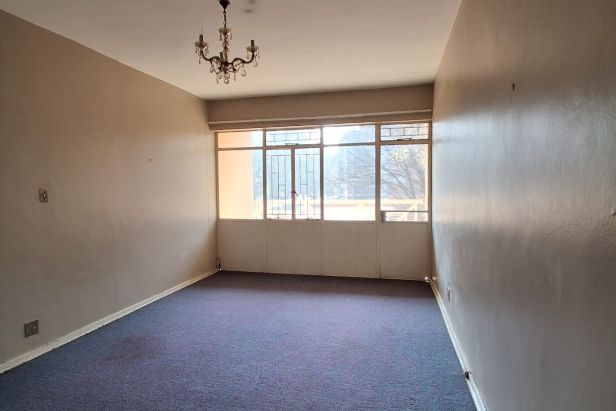 A spacious, empty living room featuring blue carpeting, neutral wall tones, and large windows providing natural light.