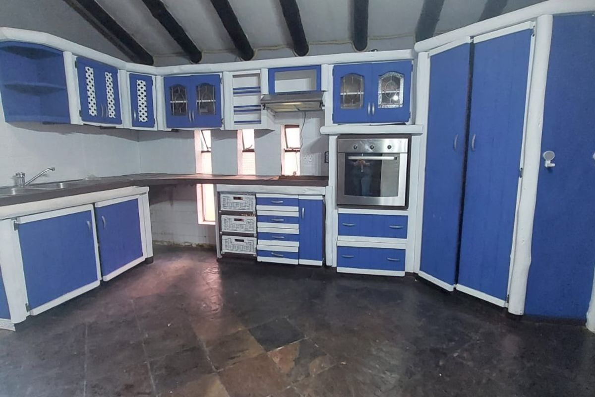 A rustic kitchen featuring blue cabinetry, built-in oven, extractor fan, and exposed ceiling beams with dark tiled flooring.