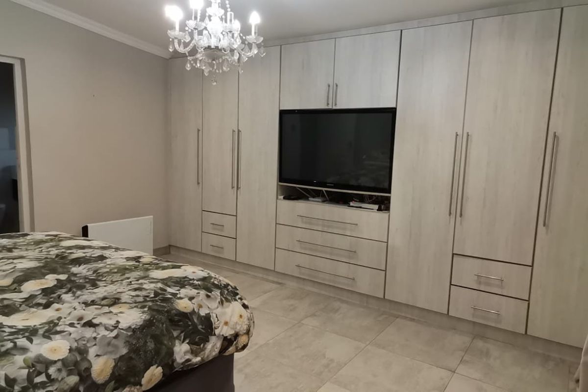 Spacious bedroom featuring extensive built-in cabinetry with integrated media storage and direct access to an en-suite bathroom.