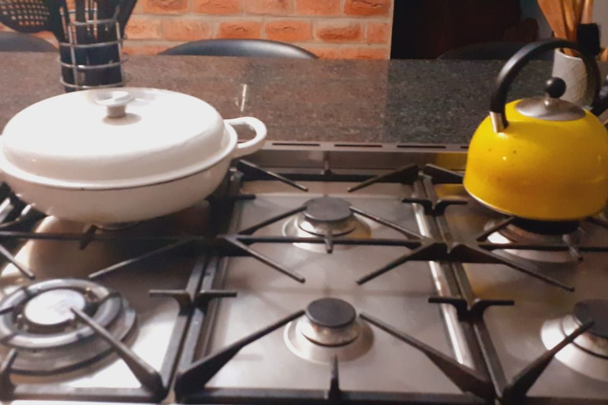 A close-up view of a stainless steel gas cooktop set into a dark granite countertop with an exposed brick feature wall in the background.
