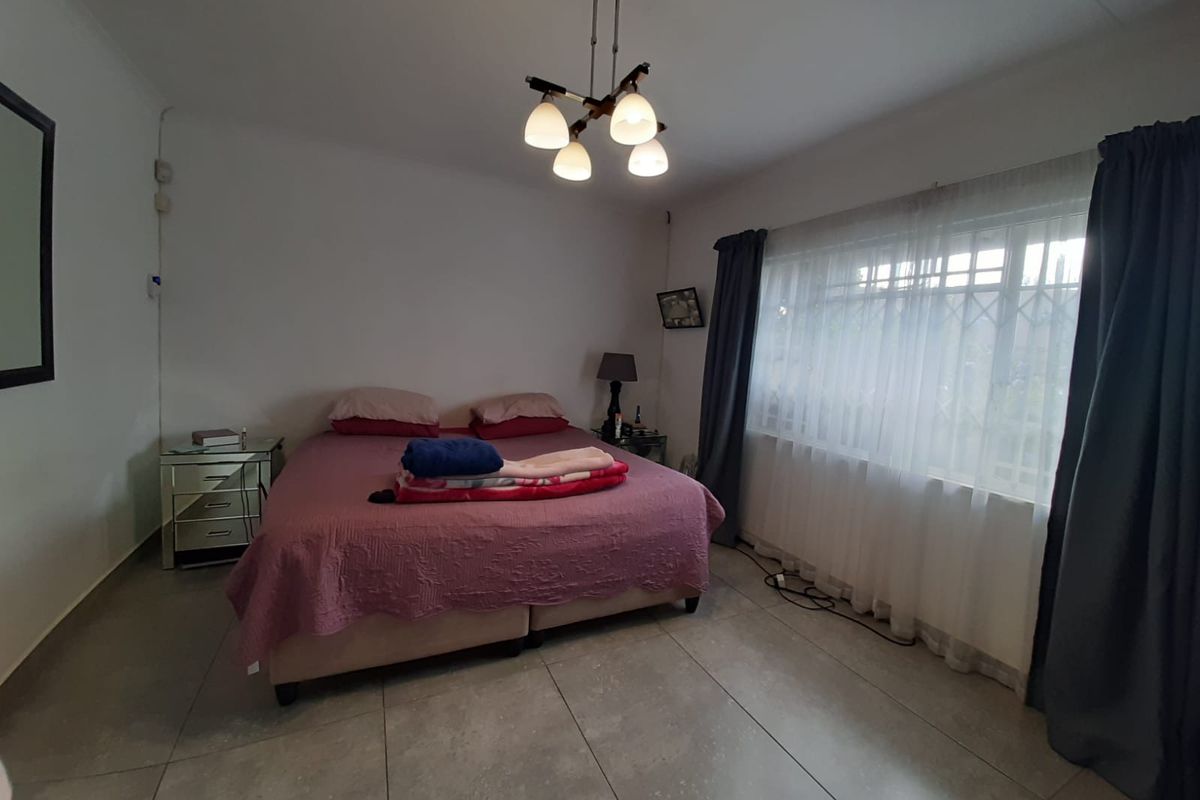 A spacious bedroom featuring large format floor tiles, a central pendant light fixture, and a window fitted with security bars.