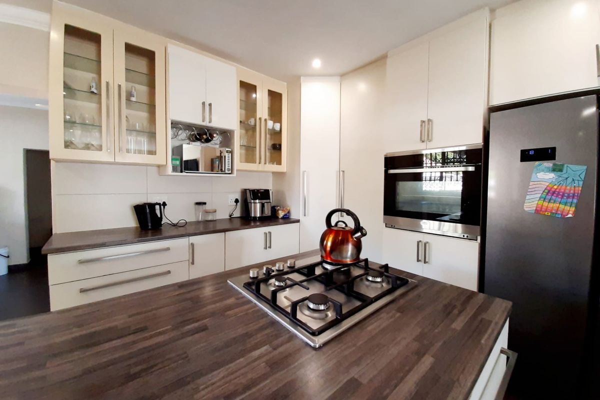 Modern kitchen featuring a central island with a built-in gas hob, dark wood-look countertops, and ample white cabinetry with glass-front display units.