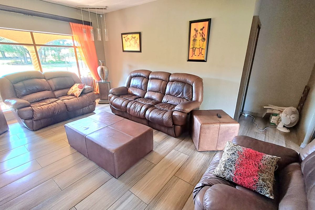 A spacious living room featuring large windows with natural light, wood-look ceramic floor tiles, and a neutral wall finish.