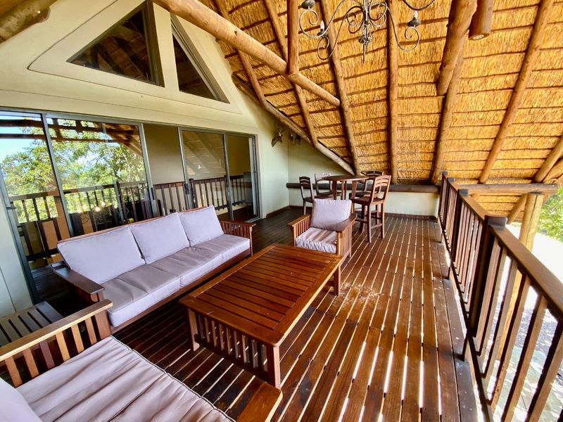 Spacious covered balcony featuring a traditional thatched roof, exposed timber rafters, and timber decking, offering an ideal outdoor entertainment area.