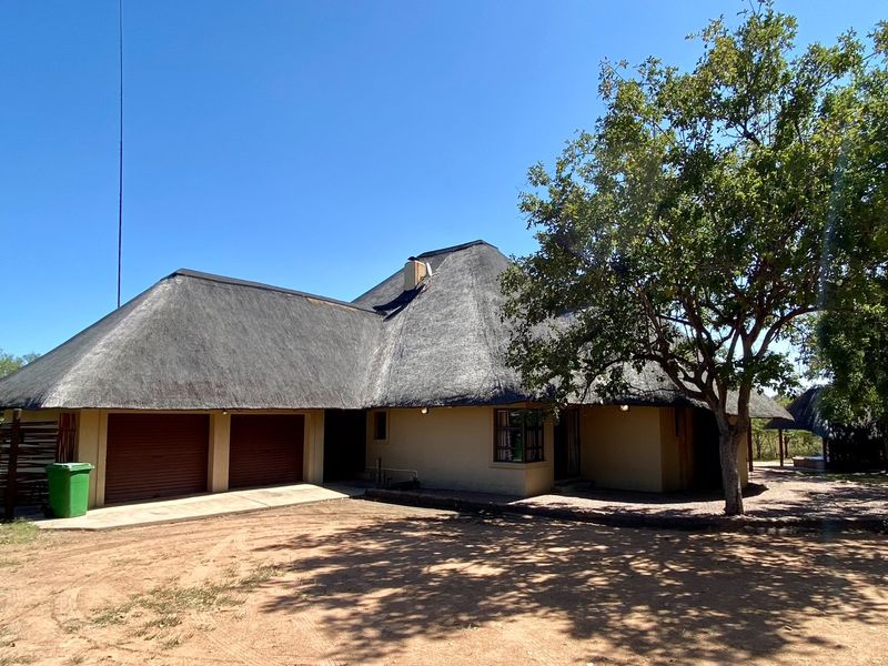 Front view of a single-story house featuring a traditional thatch roof, double garage with roll-up doors, and a paved driveway area.
