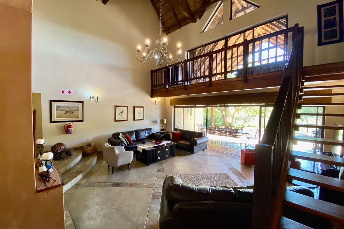 Spacious double-volume living area featuring a vaulted thatched ceiling, exposed timber rafters, a mezzanine level, and large sliding doors opening to the outdoors.