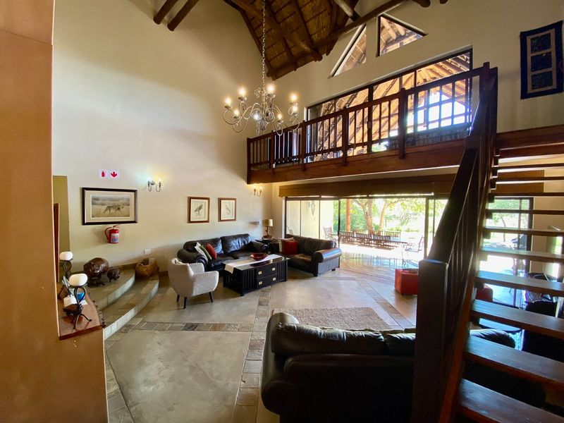 Spacious double-volume living area featuring a vaulted thatched ceiling, exposed timber rafters, a mezzanine level, and large sliding doors opening to the outdoors.