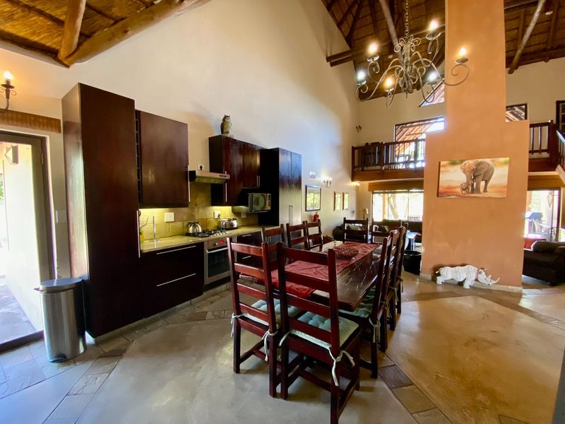 Spacious open-plan kitchen and dining area featuring high vaulted thatched ceilings, exposed timber beams, dark wood cabinetry, and a mezzanine level overlooking the space.